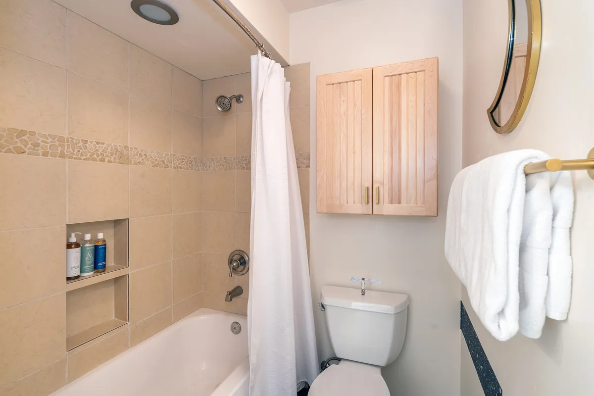 A tranquil bathroom featuring a bathtub with shower curtain, wooden cabinets, and a towel rack adorned with high-quality towels. The soft lighting and soothing color palette create a calming, private retreat ideal for relaxation and self-care routines.