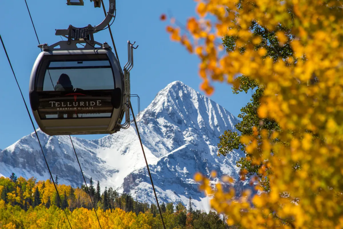 A striking view of Telluride’s iconic gondola gliding above snow-capped mountains and colorful autumn foliage. The gondola is a focal point, signifying quick and scenic access to ski slopes and mountain adventures.
