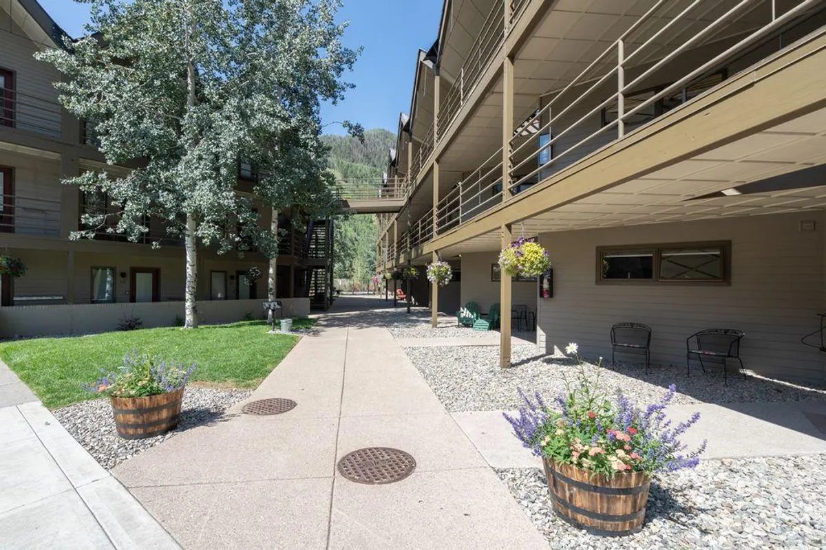 A welcoming exterior scene featuring flower pots, a walkway, building facades, and mature trees provides a sense of community and access. The inviting atmosphere underscores the property's walkability and downtown connection.