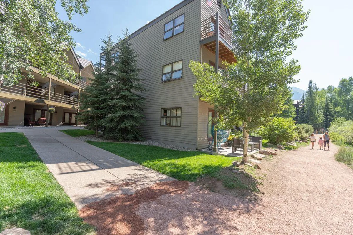 A serene, welcoming exterior view of the building’s facade with a gentle pathway winding through surrounding greenery. The environment feels peaceful and connected to nature, highlighting the ease of stepping outside or walking to nearby amenities.